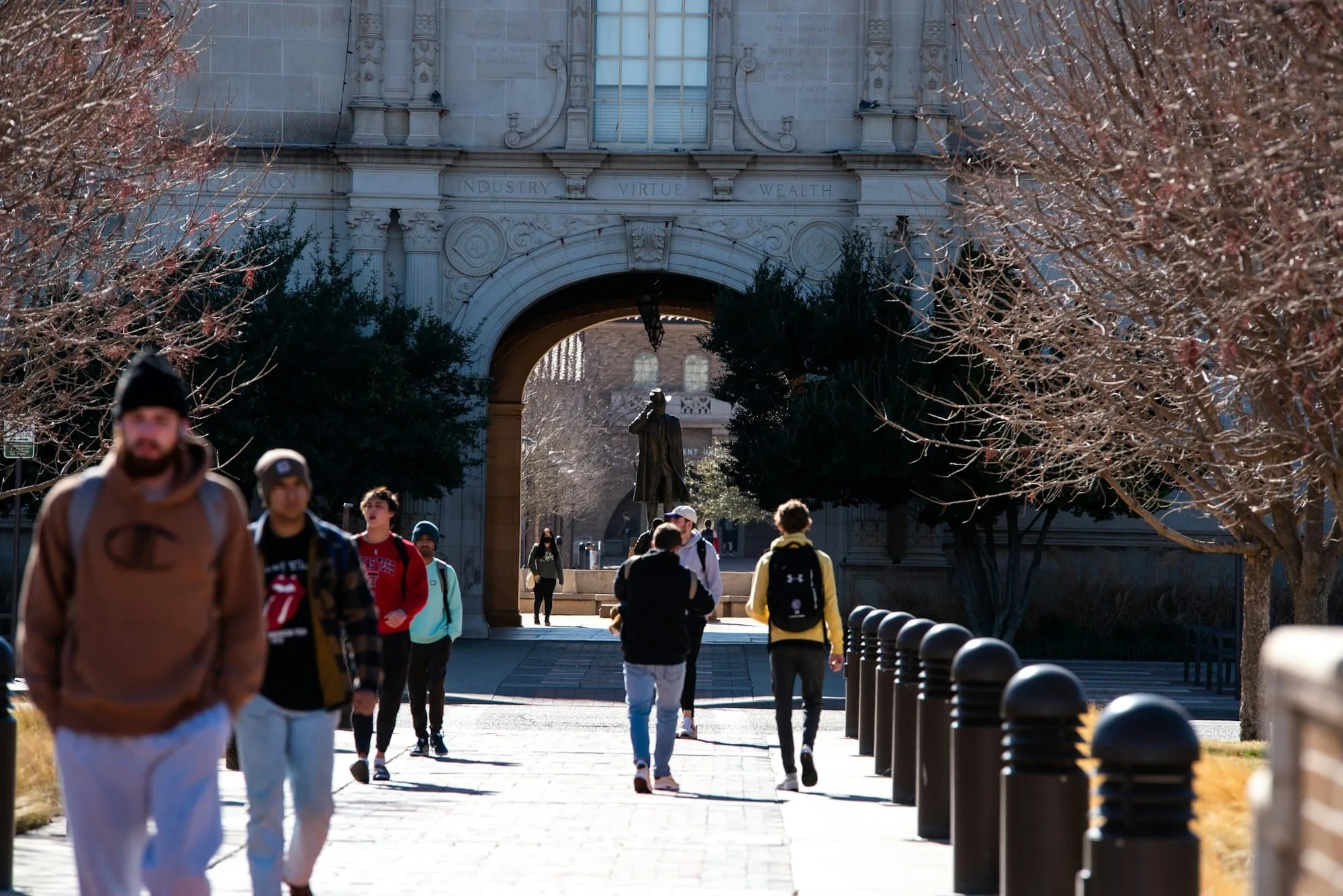 Students walking along a path towards a stone archway on a university campus